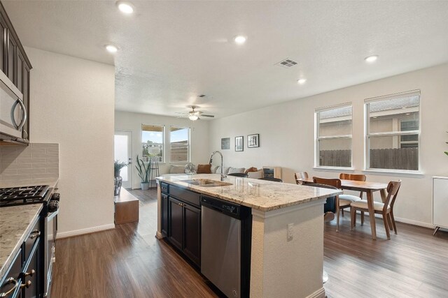 kitchen featuring appliances with stainless steel finishes, a sink, dark wood-style floors, a ceiling fan, and light stone countertops