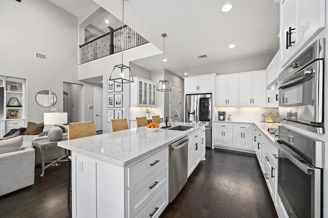 kitchen featuring light stone counters, a sink, stainless steel appliances, white cabinets, and visible vents