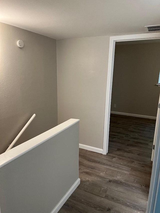 hall featuring visible vents, baseboards, dark wood-style flooring, and an upstairs landing