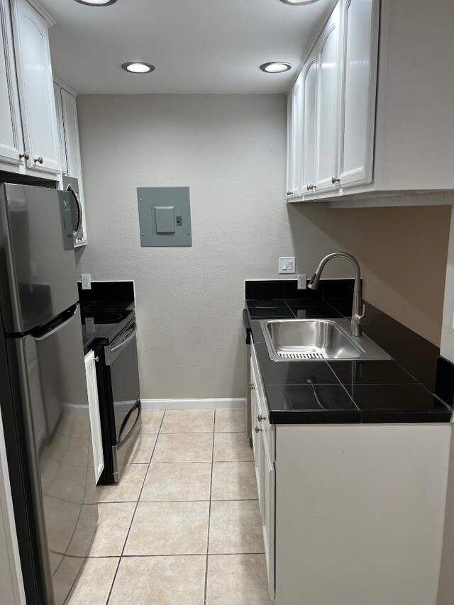 kitchen featuring dark countertops, a sink, electric panel, stainless steel appliances, and white cabinets