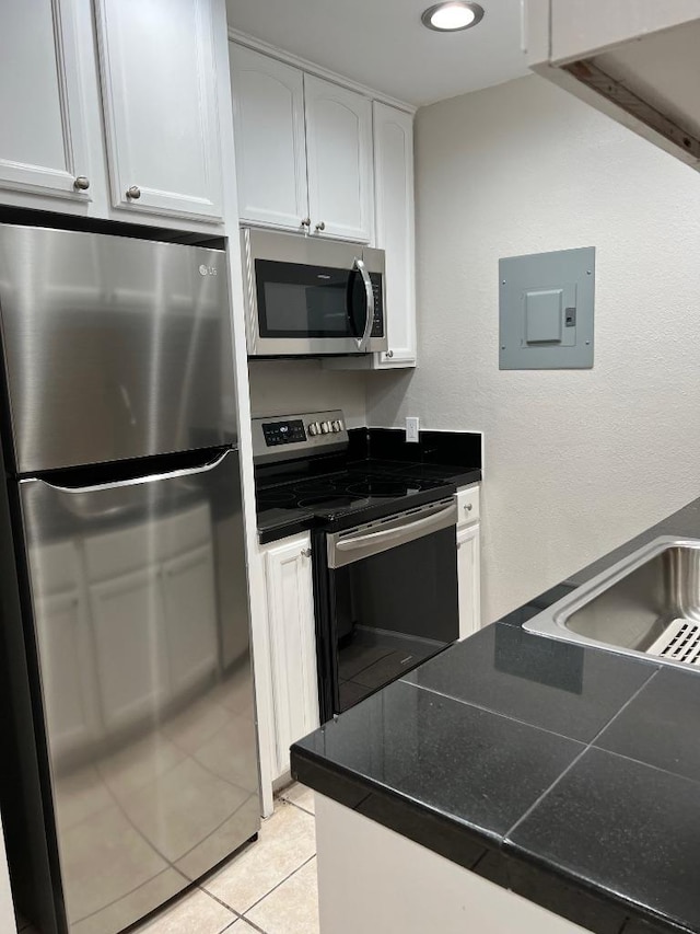 kitchen with white cabinets, electric panel, light tile patterned floors, dark countertops, and appliances with stainless steel finishes