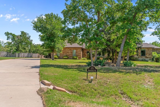 view of property hidden behind natural elements with stone siding, a front yard, and fence