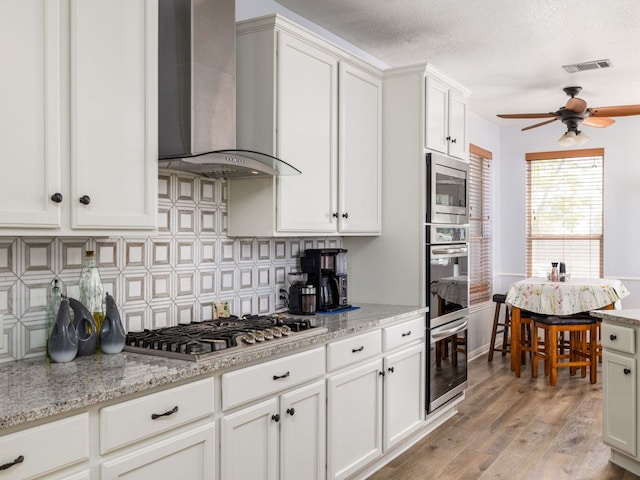 16019 Dark Ln, Austin, TX 78717 - kitchen with wall chimney exhaust hood, stainless steel appliances, a ceiling fan, backsplash, and light wood finished floors