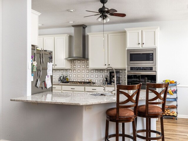 16019 Dark Ln, Austin, TX 78717 - kitchen featuring stainless steel appliances, wall chimney exhaust hood, a ceiling fan, decorative backsplash, and a kitchen breakfast bar