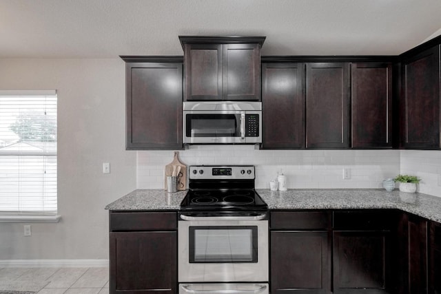 kitchen featuring stainless steel appliances, tasteful backsplash, baseboards, dark brown cabinetry, and light stone countertops