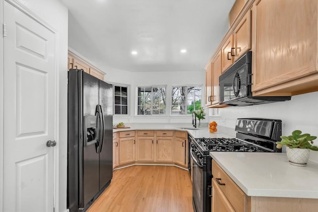 kitchen featuring light brown cabinetry, a sink, light wood-style floors, light countertops, and black appliances