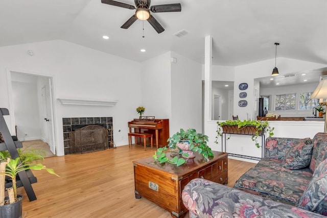 living area featuring a tiled fireplace, visible vents, lofted ceiling, a ceiling fan, and wood finished floors
