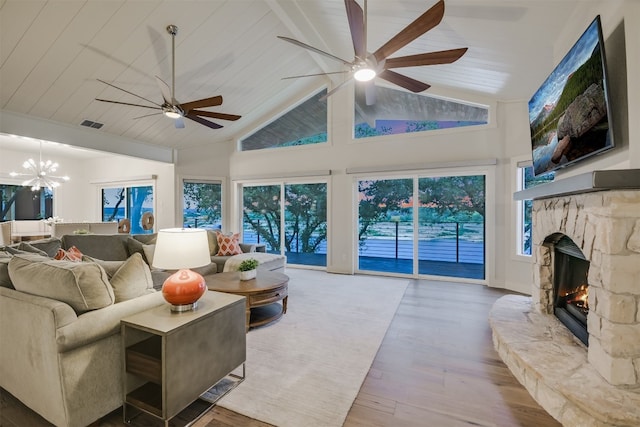 living room featuring high vaulted ceiling, wood finished floors, a stone fireplace, ceiling fan with notable chandelier, and visible vents