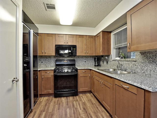 8411 Glen Canyon Dr, Round Rock, TX 78681 - kitchen featuring black appliances, a sink, light wood-style floors, brown cabinets, and a textured ceiling