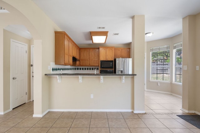 13321 Kirkglen Dr, Austin, TX 78727 - kitchen featuring black microwave, stainless steel refrigerator with ice dispenser, arched walkways, light tile patterned floors, and a breakfast bar area