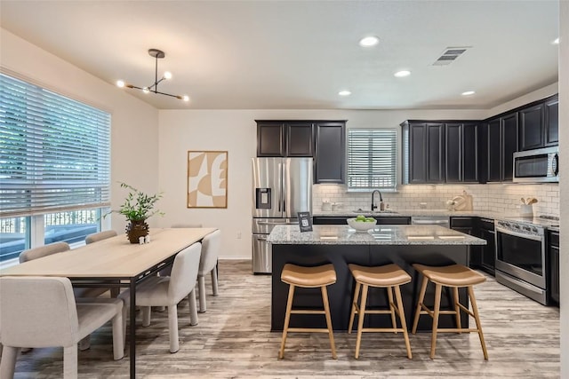 kitchen with a center island, light stone counters, tasteful backsplash, light wood-style floors, and stainless steel appliances