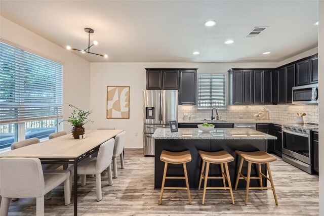 10504 Abana Way, Austin, TX 78748 - kitchen featuring stainless steel appliances, light wood-style floors, light stone counters, a center island, and backsplash