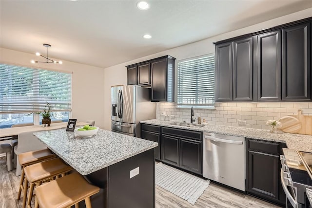 kitchen featuring stainless steel appliances, backsplash, a sink, light wood-style floors, and a kitchen island