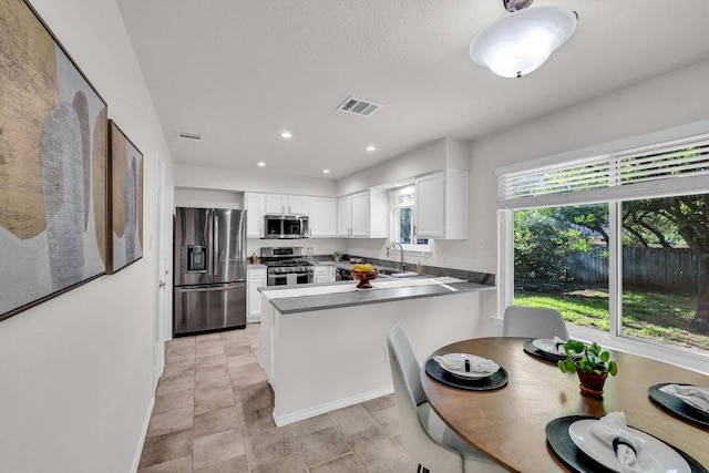 6906 Tesoro Trl, Austin, TX 78729 - kitchen with stainless steel appliances, a peninsula, white cabinets, a sink, and recessed lighting