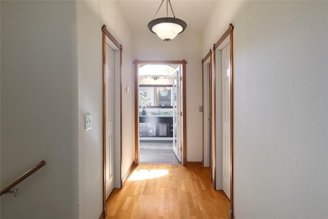 corridor featuring a barn door, baseboards, a sink, and light wood-style flooring