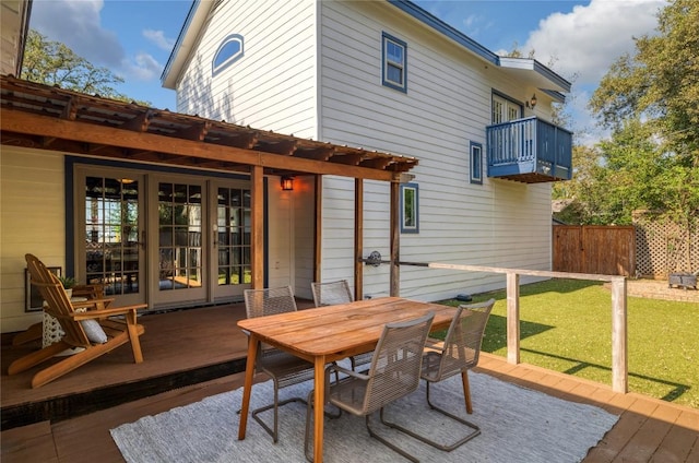 back of property with fence, a balcony, outdoor dining space, a lawn, and a deck