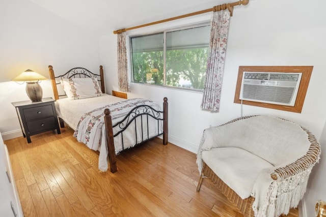bedroom with a wall mounted air conditioner, baseboards, and light wood-type flooring