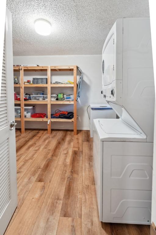 laundry area with light wood-type flooring, stacked washing maching and dryer, laundry area, and a textured ceiling