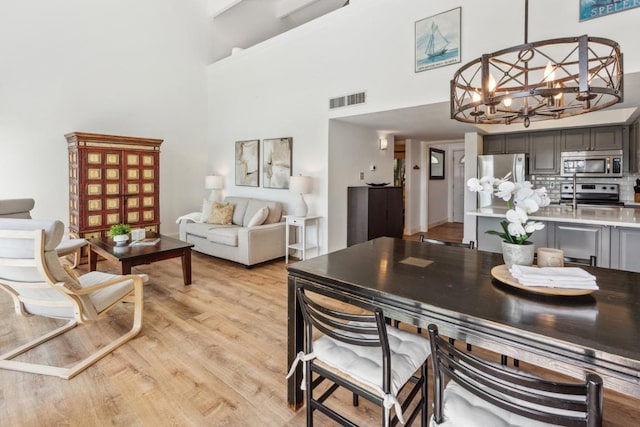 dining space with light wood-style flooring, visible vents, a high ceiling, and a notable chandelier