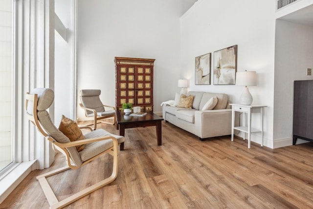 living area with light wood finished floors, baseboards, a high ceiling, and visible vents