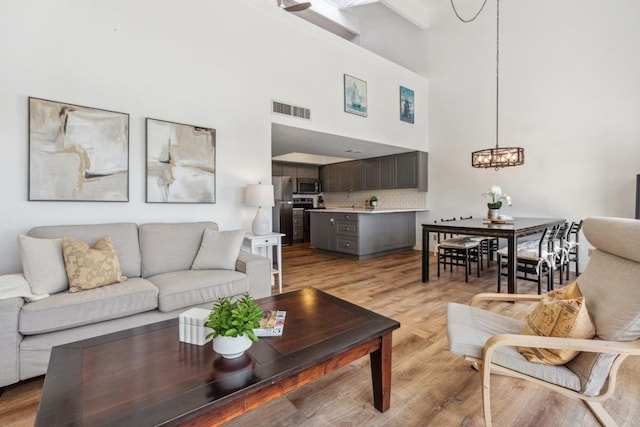 living room featuring a towering ceiling, visible vents, an inviting chandelier, and light wood-style floors