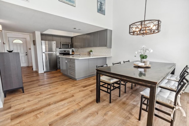 dining area featuring light wood-type flooring, a high ceiling, a notable chandelier, and visible vents