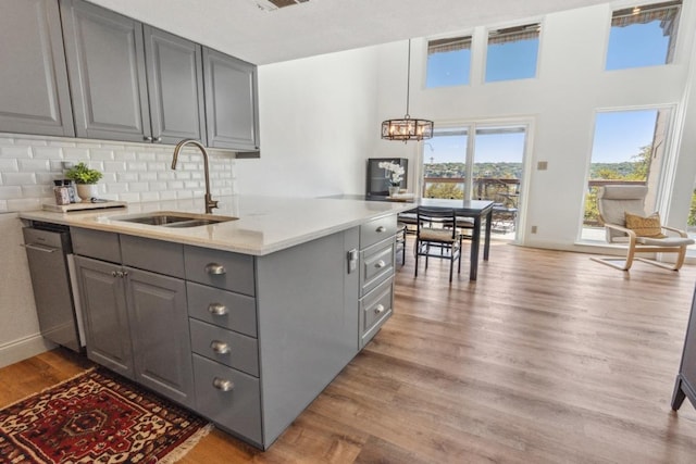 kitchen featuring a sink, dishwasher, light wood finished floors, light countertops, and gray cabinetry