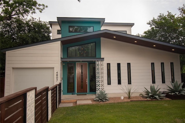 modern home featuring a garage, a front yard, and fence