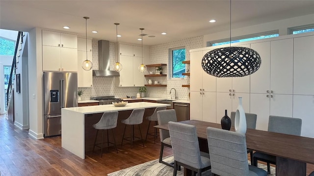 kitchen featuring wall chimney exhaust hood, stainless steel appliances, a center island, a sink, and dark wood-style flooring