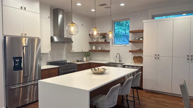kitchen with premium appliances, open shelves, light countertops, a sink, and wall chimney exhaust hood