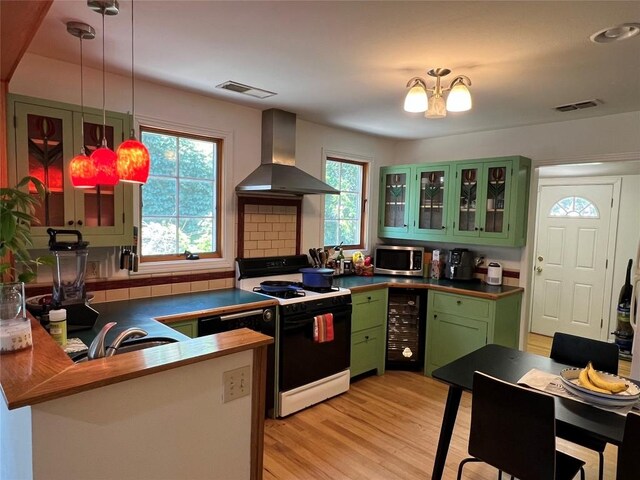 kitchen with stainless steel microwave, visible vents, gas stove, green cabinets, and wall chimney range hood