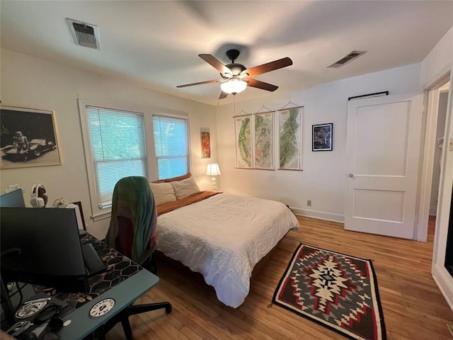 bedroom featuring baseboards, a ceiling fan, wood finished floors, and visible vents