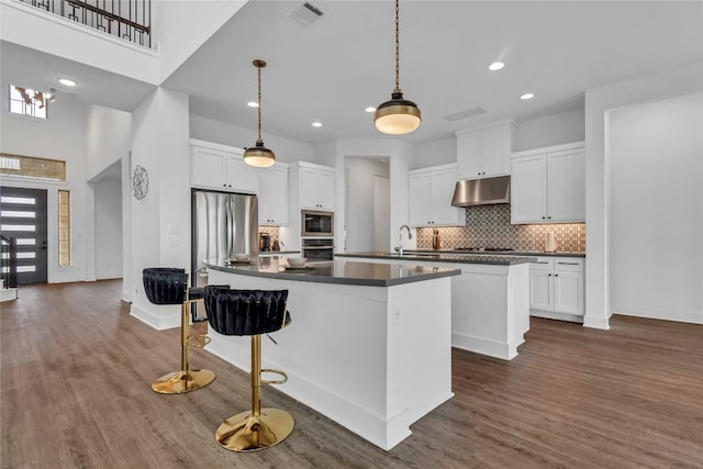 2616 War Wagon Way, Leander, TX 78641 - kitchen with an island with sink, appliances with stainless steel finishes, dark countertops, under cabinet range hood, and tasteful backsplash