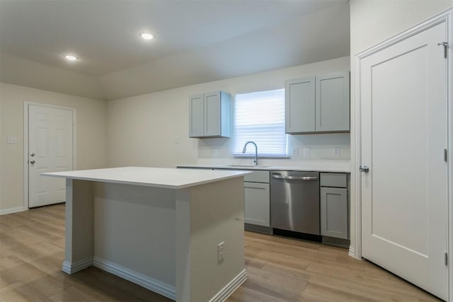 kitchen featuring a sink, dishwasher, light wood finished floors, gray cabinetry, and a kitchen island