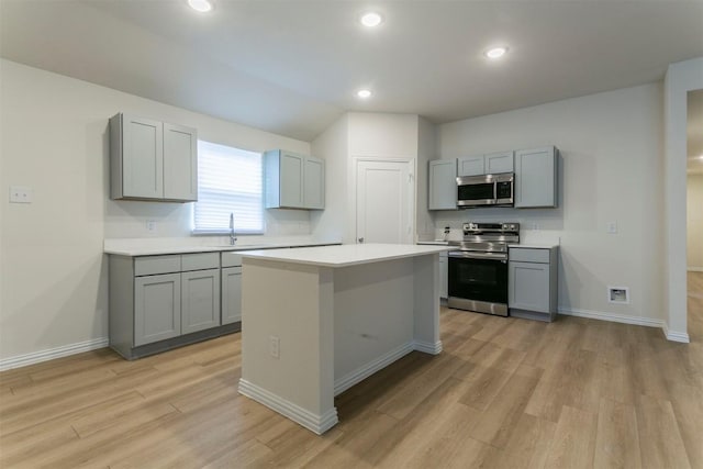 kitchen featuring stainless steel appliances, a sink, light wood-style floors, gray cabinetry, and light countertops