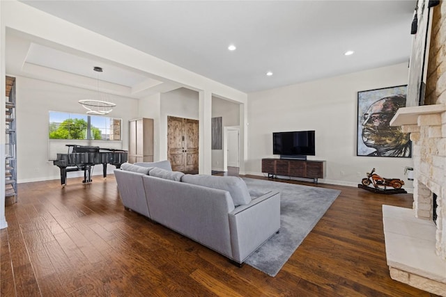 living area with a tray ceiling, baseboards, dark wood-style floors, and a stone fireplace
