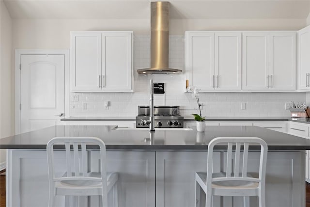 kitchen with white cabinets, dark countertops, tasteful backsplash, and wall chimney range hood