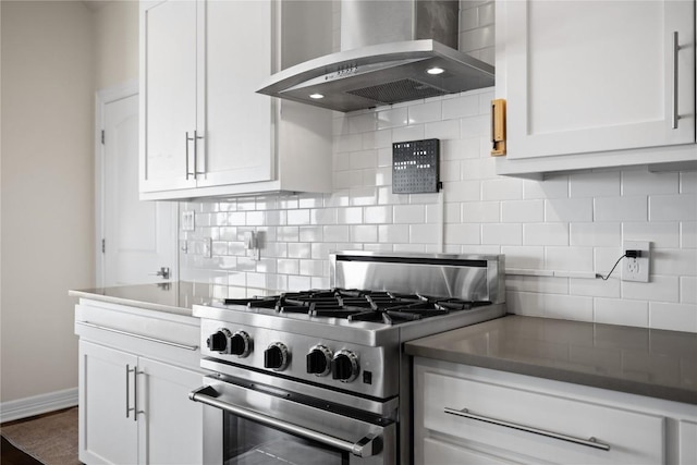kitchen with baseboards, white cabinetry, decorative backsplash, gas stove, and wall chimney range hood