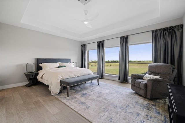 bedroom with baseboards, wood finished floors, visible vents, and a raised ceiling