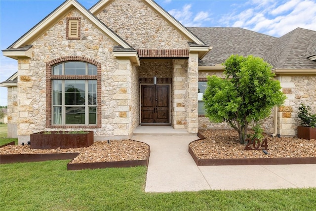 view of exterior entry with stone siding, a shingled roof, and a yard