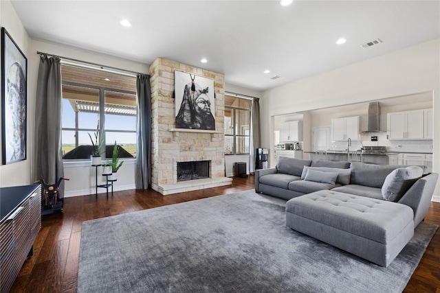 living room with recessed lighting, dark wood-style floors, a stone fireplace, visible vents, and baseboards