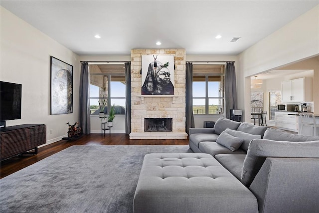 living room with recessed lighting, a stone fireplace, dark wood-type flooring, and baseboards