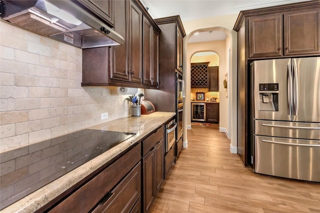 2560 Square Nail Cv, Leander, TX 78641 - kitchen featuring appliances with stainless steel finishes, wall chimney range hood, light stone countertops, light wood-style flooring, and dark brown cabinetry