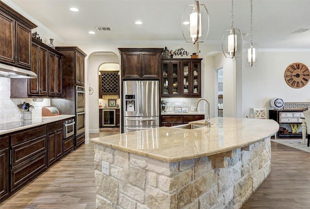 2560 Square Nail Cv, Leander, TX 78641 - kitchen with stainless steel appliances, beverage cooler, under cabinet range hood, arched walkways, and crown molding
