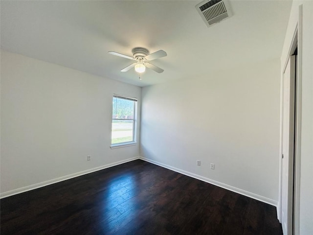 spare room with baseboards, a ceiling fan, visible vents, and dark wood finished floors