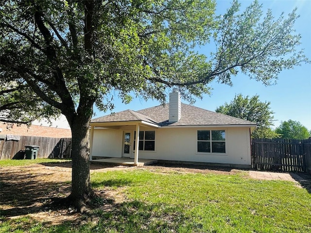 rear view of house with a patio area, a lawn, a chimney, and fence