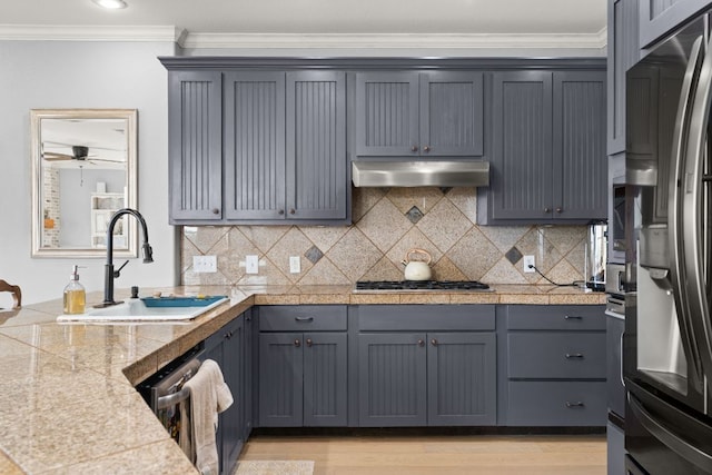 19206 Hornsby Ln, Spicewood, TX 78669 - kitchen with tile counters, appliances with stainless steel finishes, under cabinet range hood, ornamental molding, and decorative backsplash