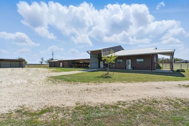 rear view of property featuring driveway, metal roof, fence, board and batten siding, and a yard