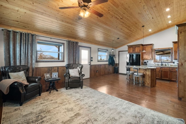 living area featuring a ceiling fan, wooden walls, wood ceiling, a wainscoted wall, and dark wood-type flooring