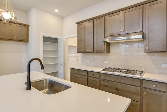 1404 S Brook Dr, Leander, TX 78641 - kitchen featuring under cabinet range hood, a sink, light countertops, backsplash, and decorative light fixtures